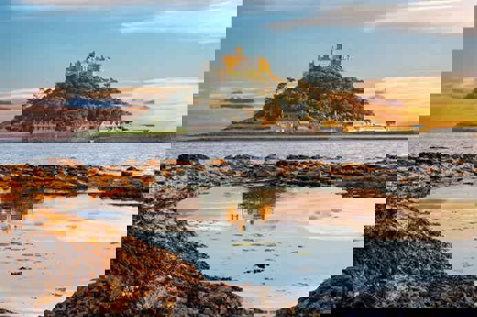 A castle ruins atop a hill on an island with the sea surrounding it at sunset