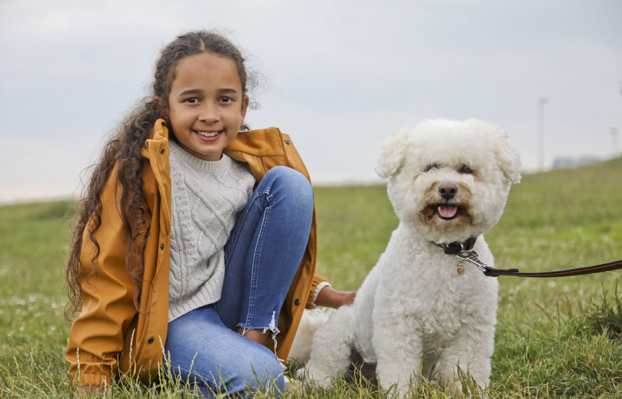 A small white fluffy dog sat in a field with a young girl