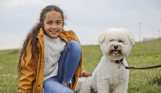A small white fluffy dog sat in a field with a young girl