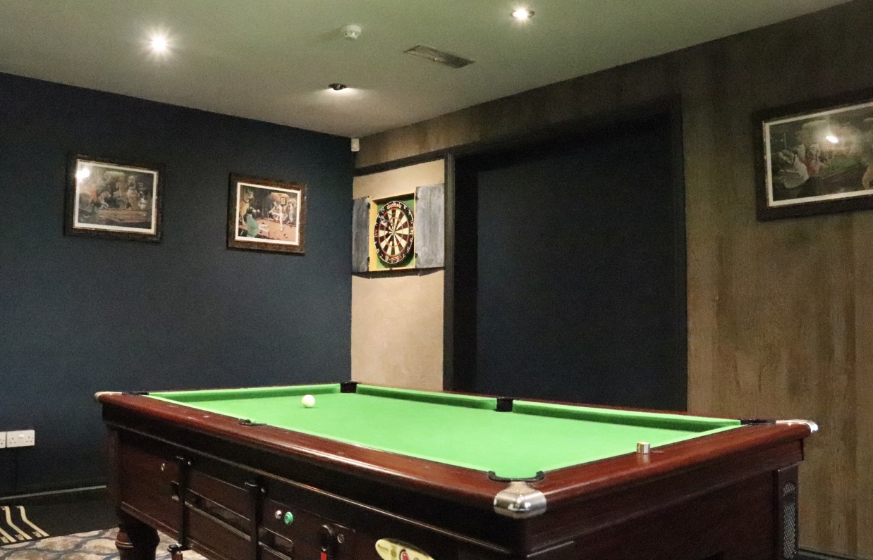 A pool table in a games room with a dart board and pictures on the walls