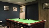 A pool table in a games room with a dart board and pictures on the walls