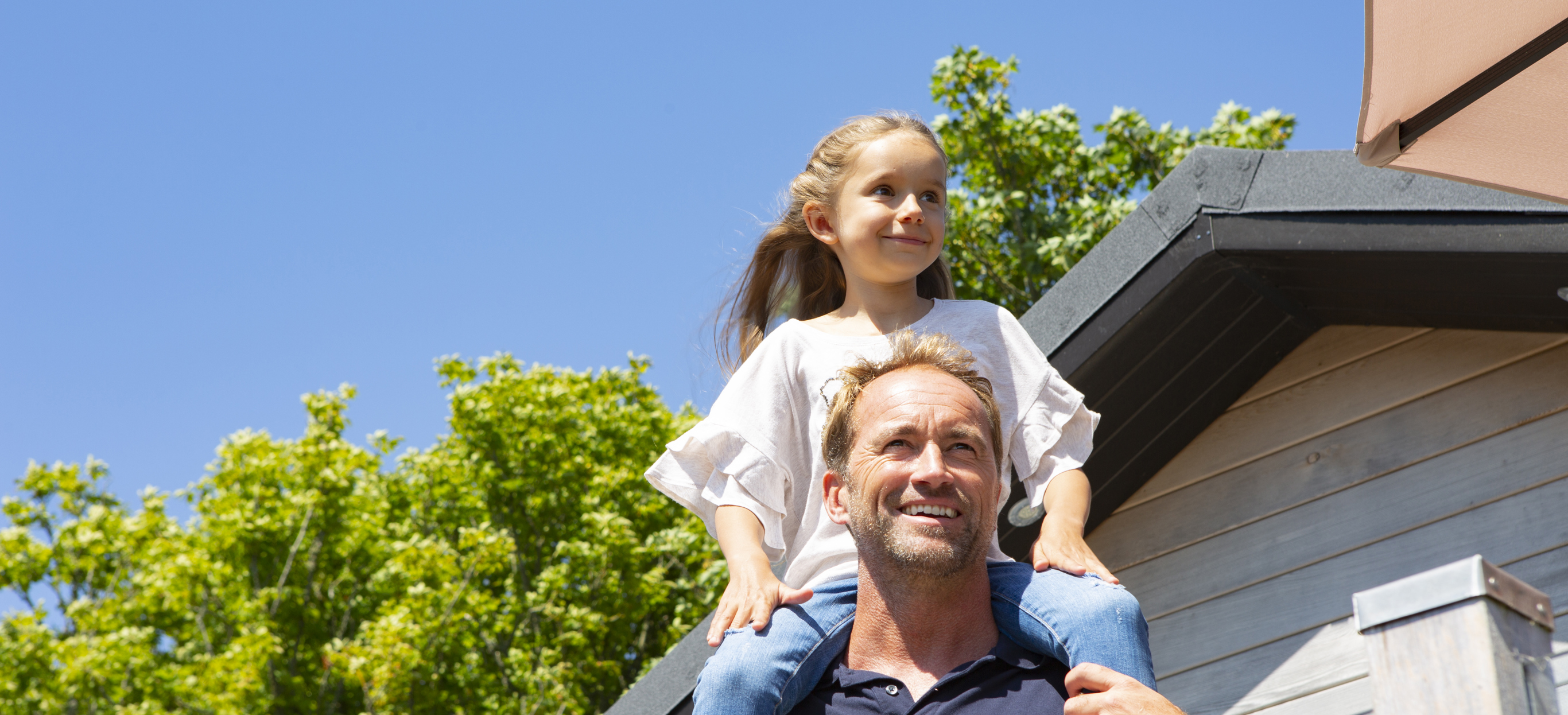 Daughter sitting on father's shoulders on the deck of their holiday lodge