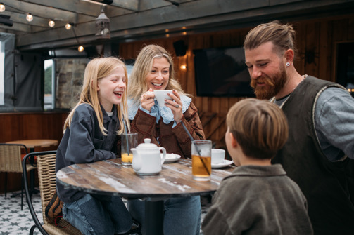 A family of four sat at a high outdoor table having a drink
