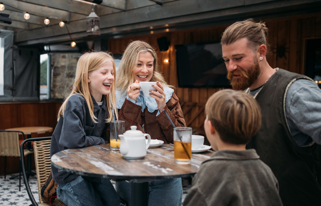 A family of four sat at a high outdoor table having a drink