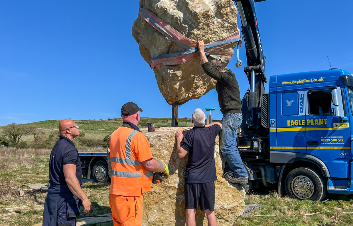 Installation of a stone sculpture in a field with blue skies