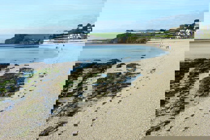 A long stretch of beach with rocky cliffside on a sunny, blue sky day