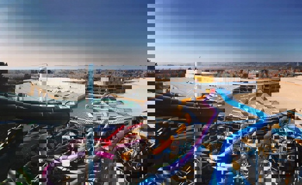 An aerial view shot of a waterpark among woodland, hills and fields with various colourful slides