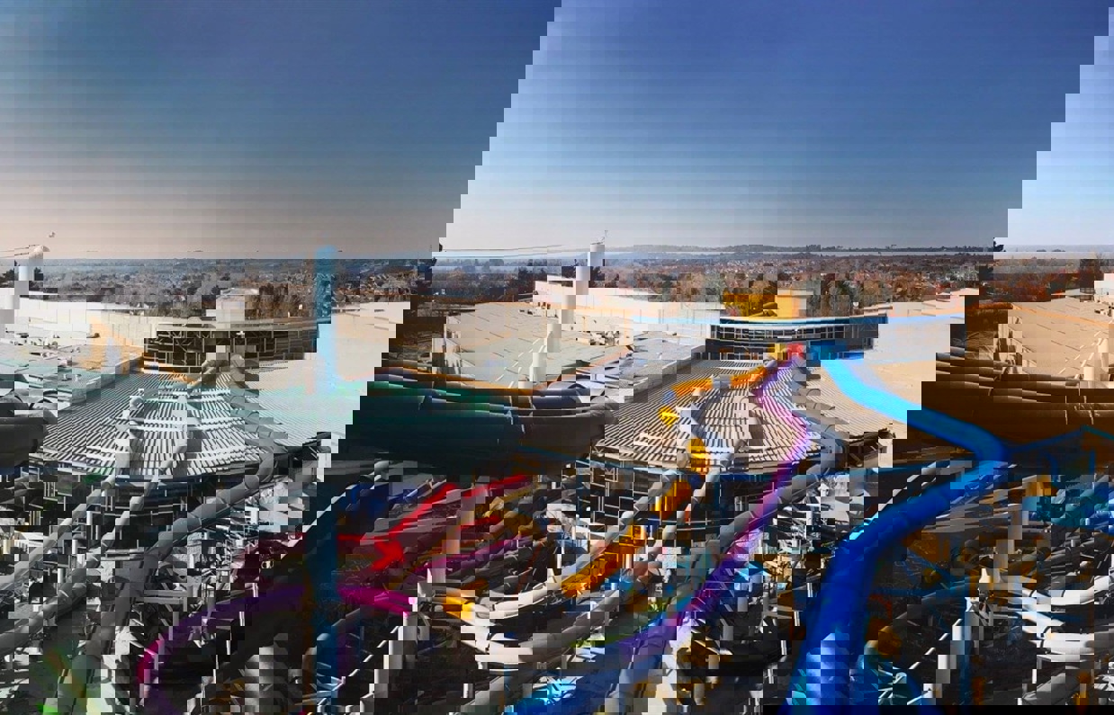 An aerial view shot of a waterpark among woodland, hills and fields with various colourful slides