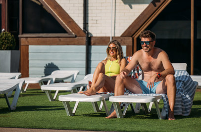 A couple sat on sun loungers in the sun smiling beside an outdoor pool