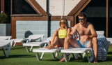A couple sat on sun loungers in the sun smiling beside an outdoor pool