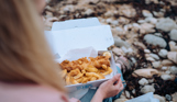 A woman sat on the beach with a fish and chip box open on her lap 