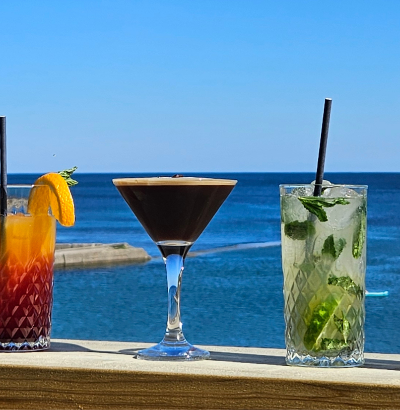 A variety of cocktails on a table with the sea as the backdrop