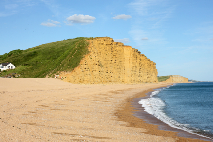 High cliffsides and grassy headlands by a sandy beach with blue sea and sky