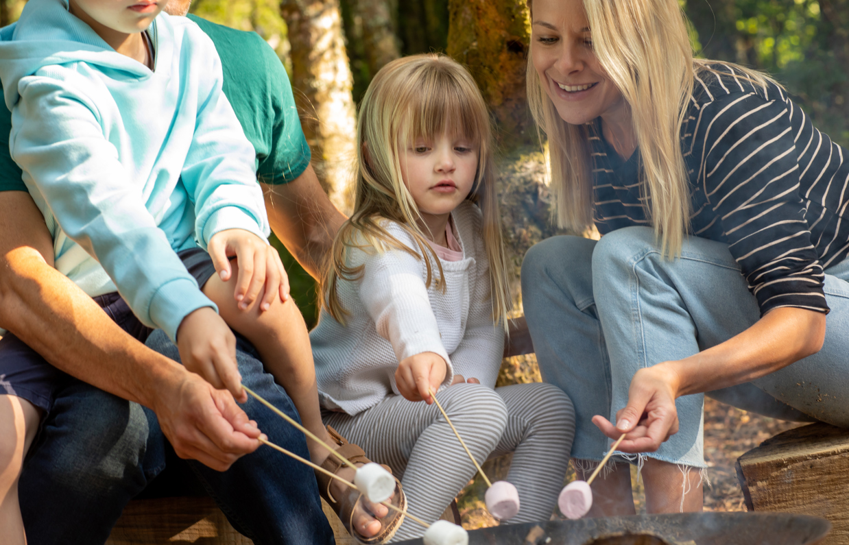 A family of four toasting marshmallows on the fire among woodland
