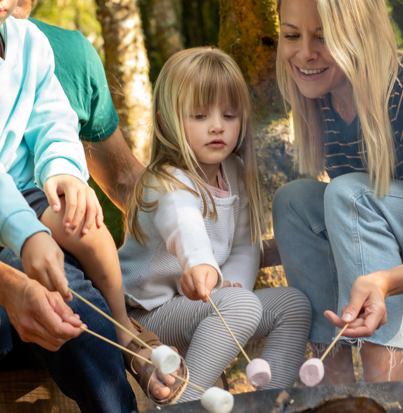 A family of four toasting marshmallows on the fire among woodland