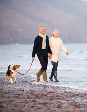 Couple walking on beach with dog in autumn