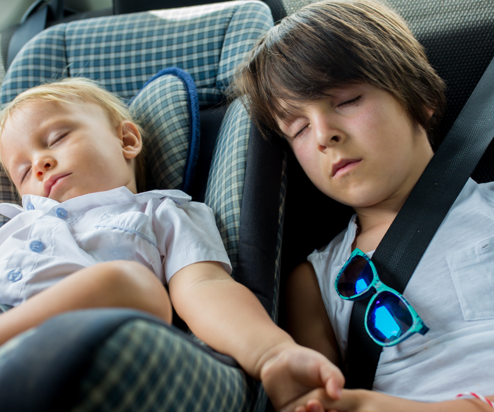 Two young children sleeping in the back of a car