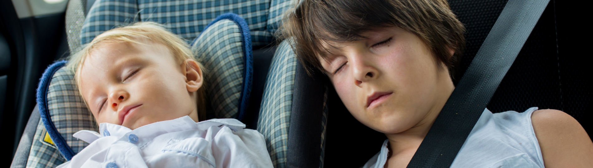 Two young children sleeping in the back of a car