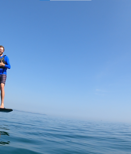 A man e-foiling on blue waters near the coast on a sunny, blue sky day
