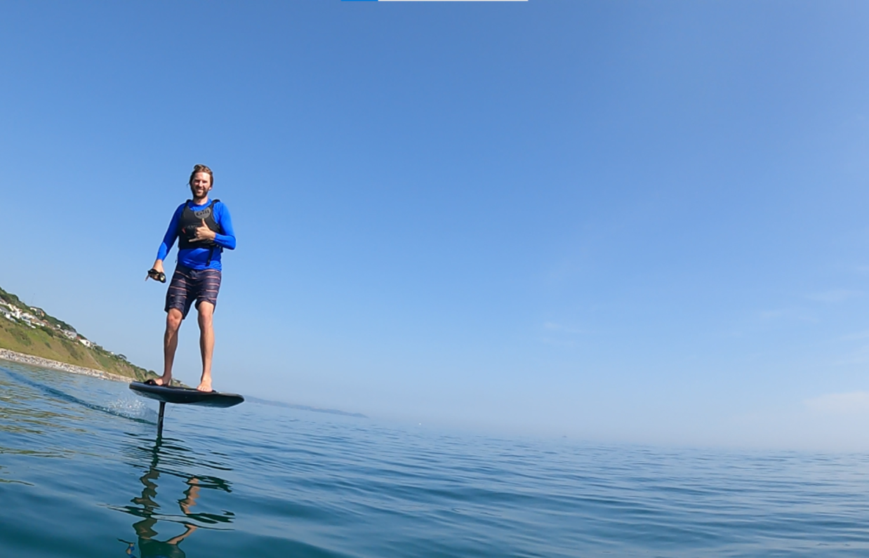 A man e-foiling on blue waters near the coast on a sunny, blue sky day