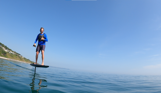 A man e-foiling on blue waters near the coast on a sunny, blue sky day