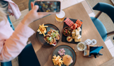 A selection of dishes including steak, burger, tacos, charcuterie board, taken from above with a woman taking a photo also from above with her iPhone
