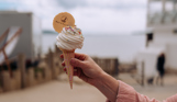 A Mr Whippy style ice cream in a cone with a Waterside wafer being held up against the backdrop of the sea