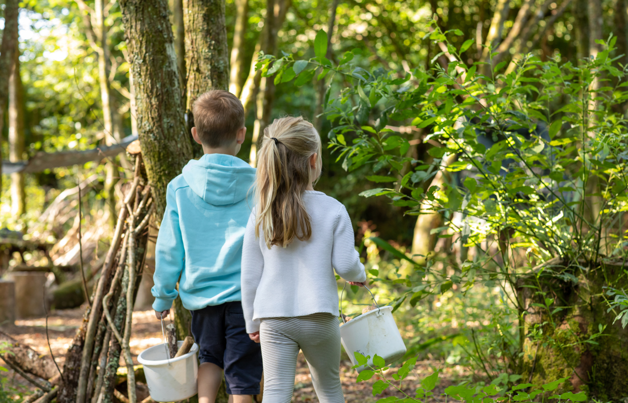 A young boy and girl walking in the woods with buckets