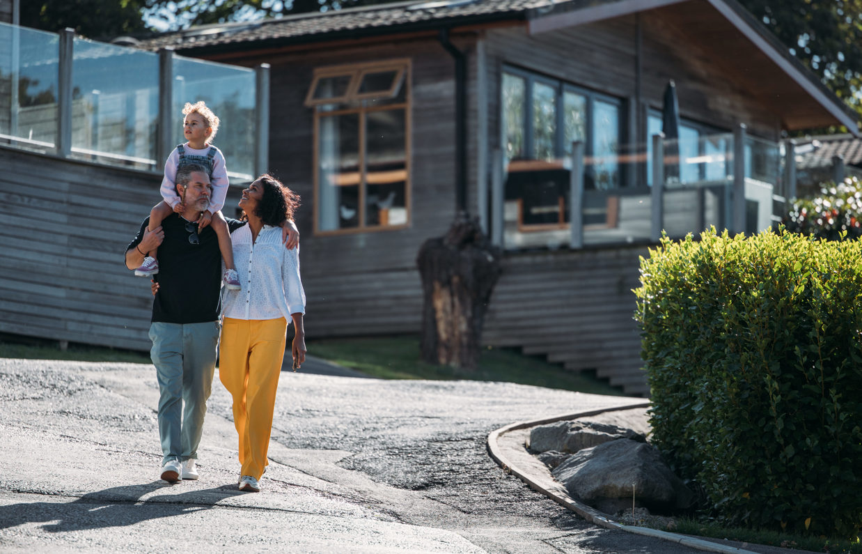A family of three walking down a road on a lodge park surrounded by holiday lodges and woodland on a sunny day