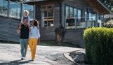 A family of three walking down a road on a lodge park surrounded by holiday lodges and woodland on a sunny day
