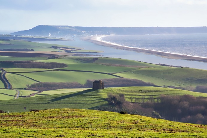 A hillfort atop a scene of rolling hills with views of Chesil Beach and the Jurassic Coast