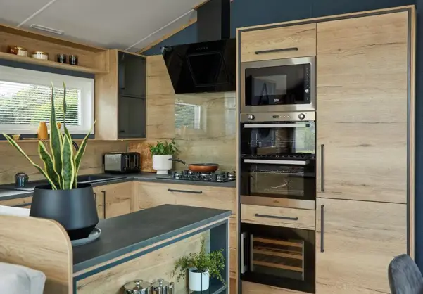 Modern kitchen and breakfast bar fitted with contemporary natural wood cupboard doors and dark blue walls