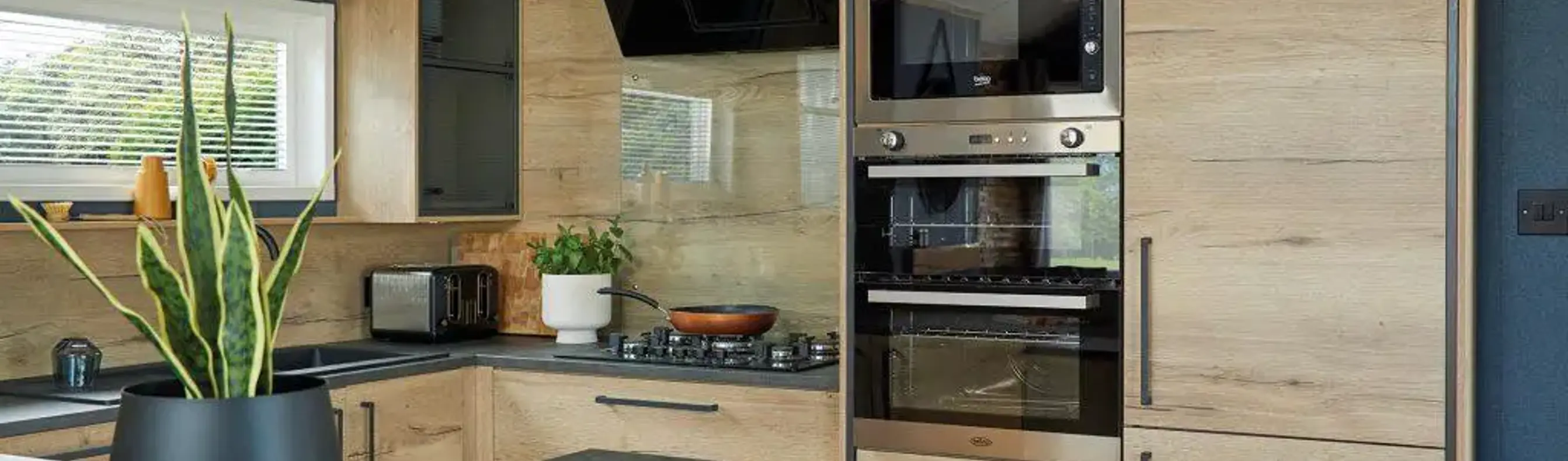 Modern kitchen and breakfast bar fitted with contemporary natural wood cupboard doors and dark blue walls