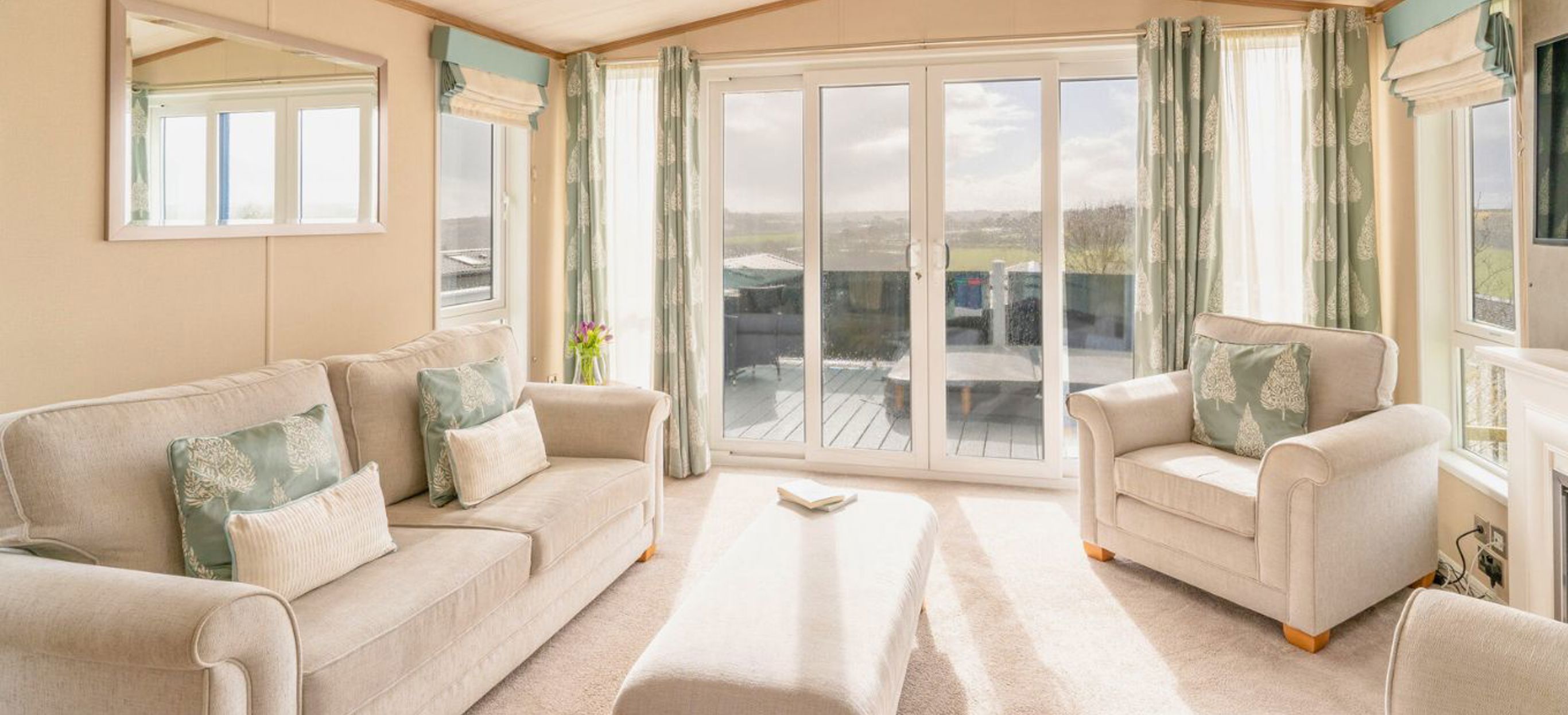 Internal of a caravan open plan living space with sliding doors onto decking with hot tub and countryside views