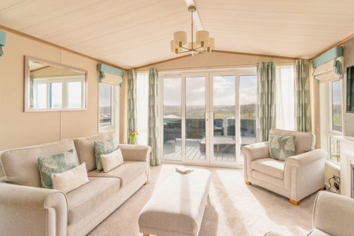 Internal of a caravan open plan living space with sliding doors onto decking with hot tub and countryside views