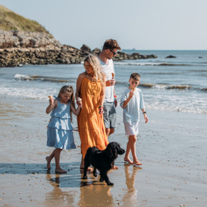Family walking a dog on the beach eating ice creams