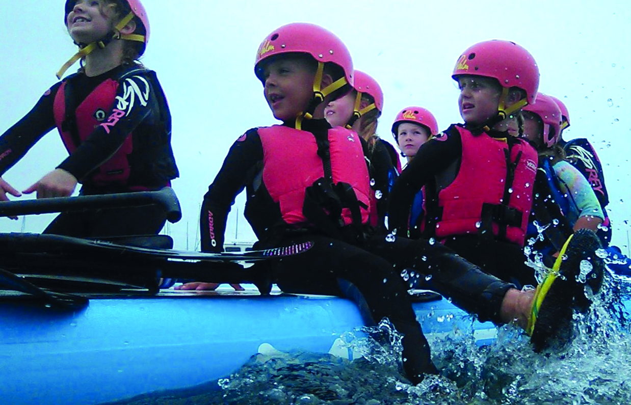 A group of children on a large paddleboard wearing water safety gear