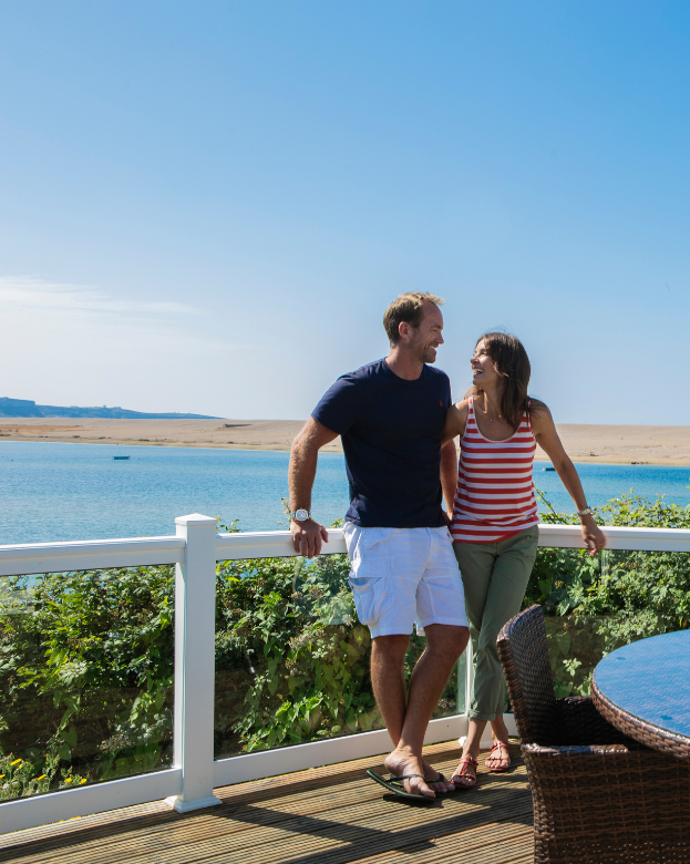 Couple on deck at Chesil Beach Holiday Park with sea and beach behind them
