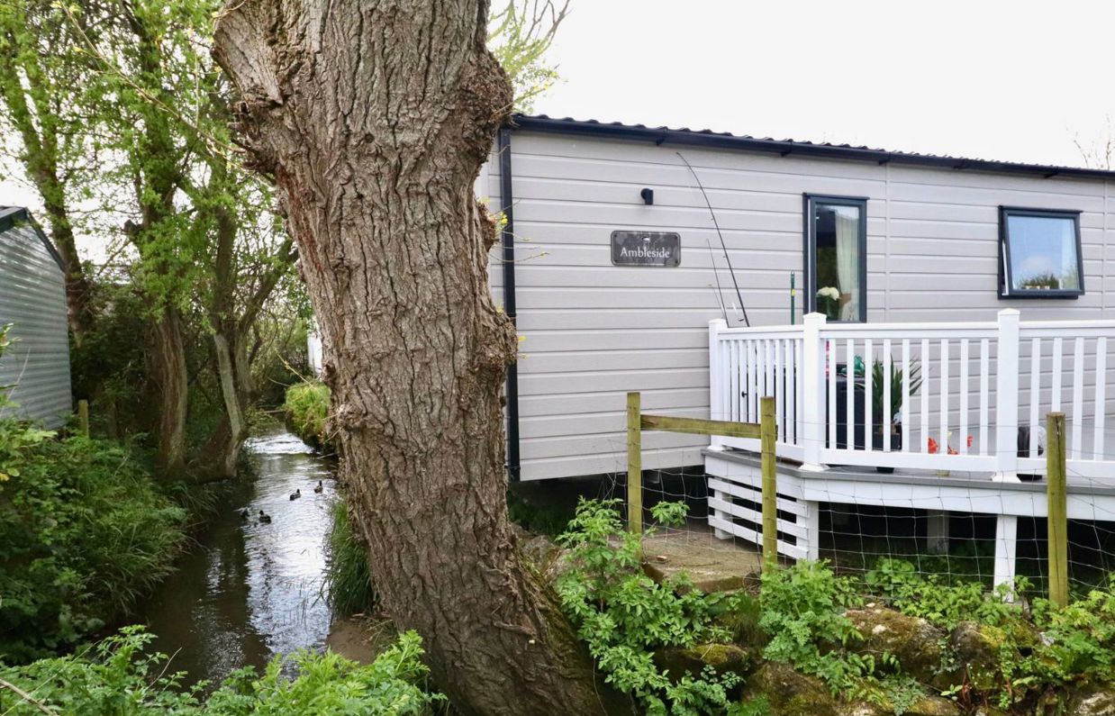 External of a caravan on pitch with decking among woodland