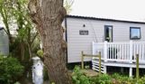 External of a caravan on pitch with decking among woodland