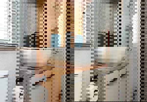 Modern shower room with large sink and shower, soft grey tiles, natural wood splashback and black fixtures