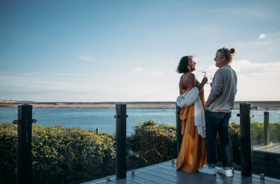 Couple toasting with sparkling wine at dusk on the deck of their lodge overlooking Chesil beach