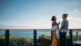 Couple toasting with sparkling wine at dusk on the deck of their lodge overlooking Chesil beach