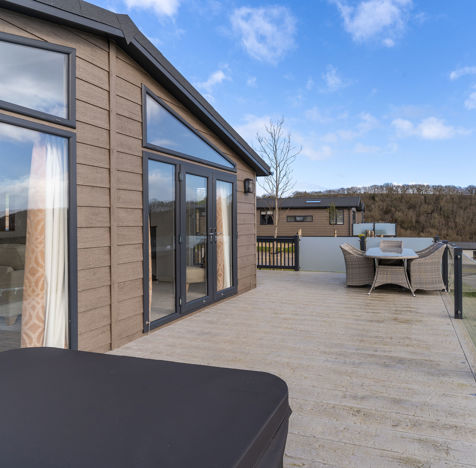 Large decking with hot tub and table and chairs outside of holiday lodge