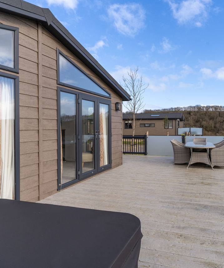 Large decking with hot tub and table and chairs outside of holiday lodge
