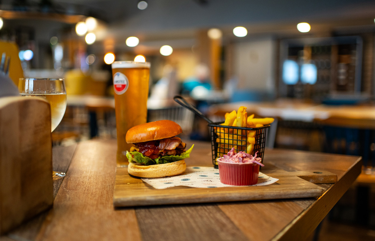 A burger, chips and coleslaw with a pint and a glass of wine in a table at Breeze Bar & Grill