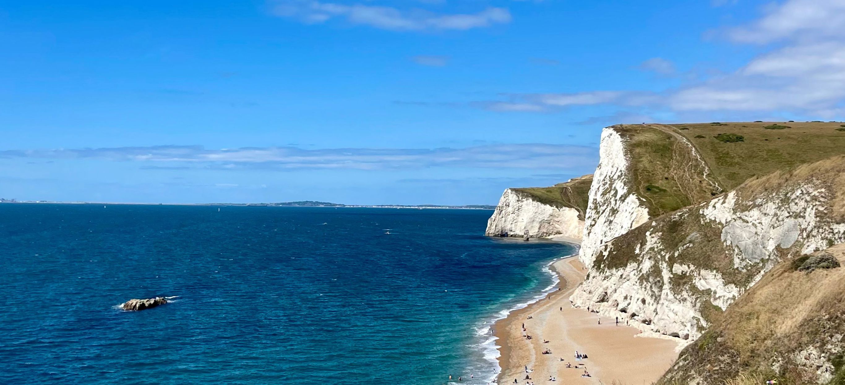 Durdle Door Beach and beyond on a sunny blue sky day with calm turquoise waters