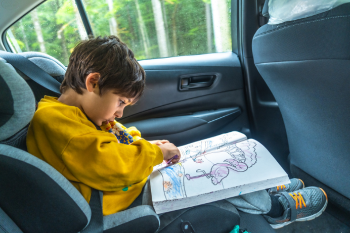 A young child drawing and colouring sat in the back of a car