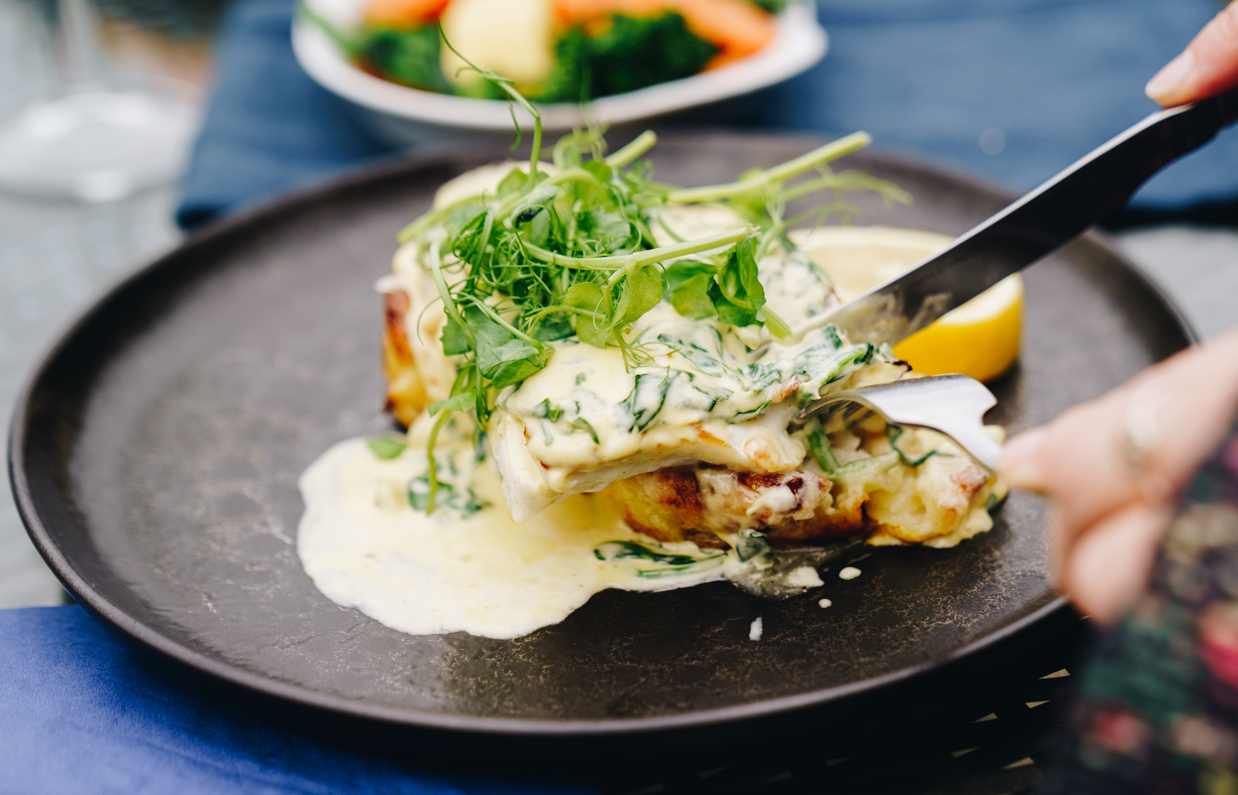 A fish dish on a black plate being eaten outside at a table