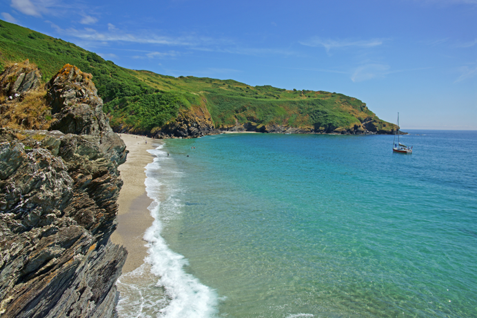 A dramatic bay with a small beach and a boat in the water surrounded by green headland